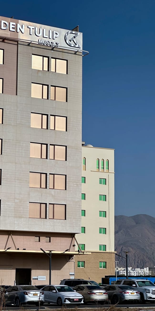 Hotel golden tulip muscat w omanie z górskim tłem i zaparkowanymi samochodami
