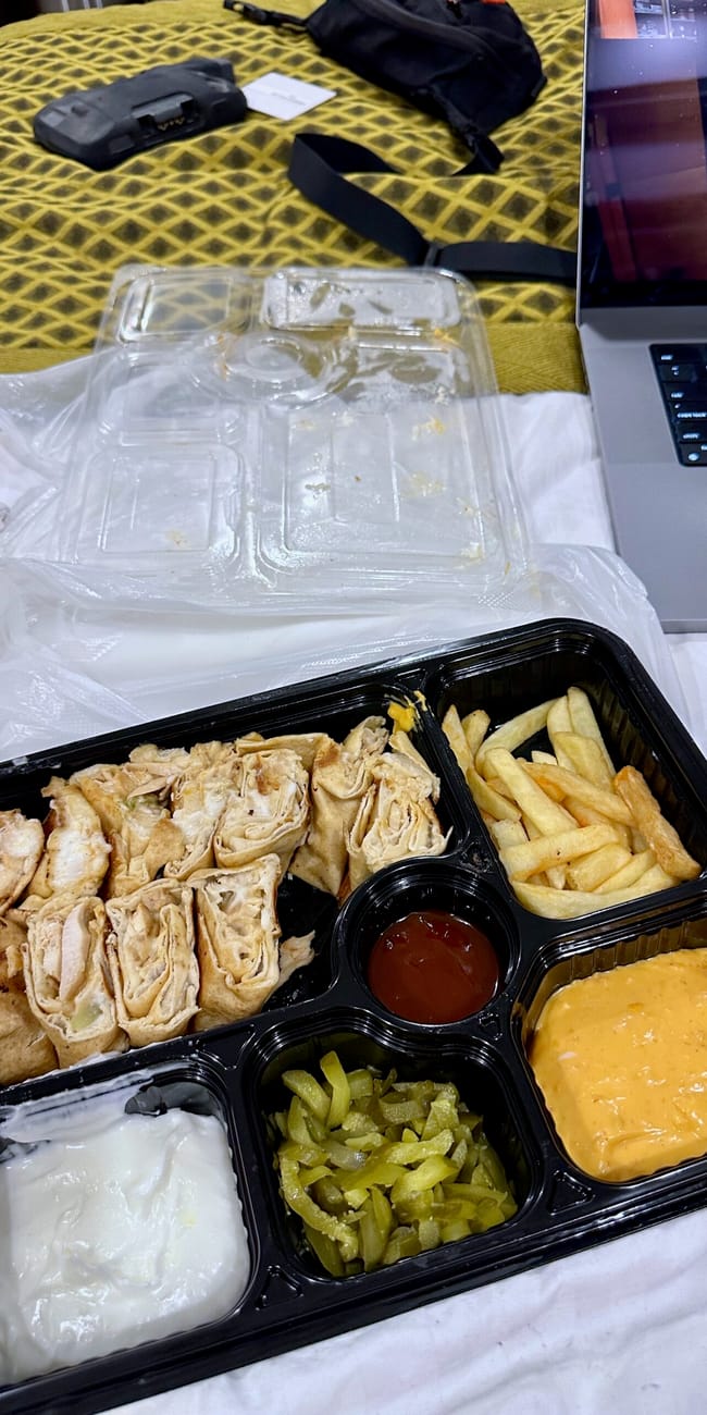 Shawarma z bagdadu z talabat z frytkami i sosami w pojemniku na stole.
