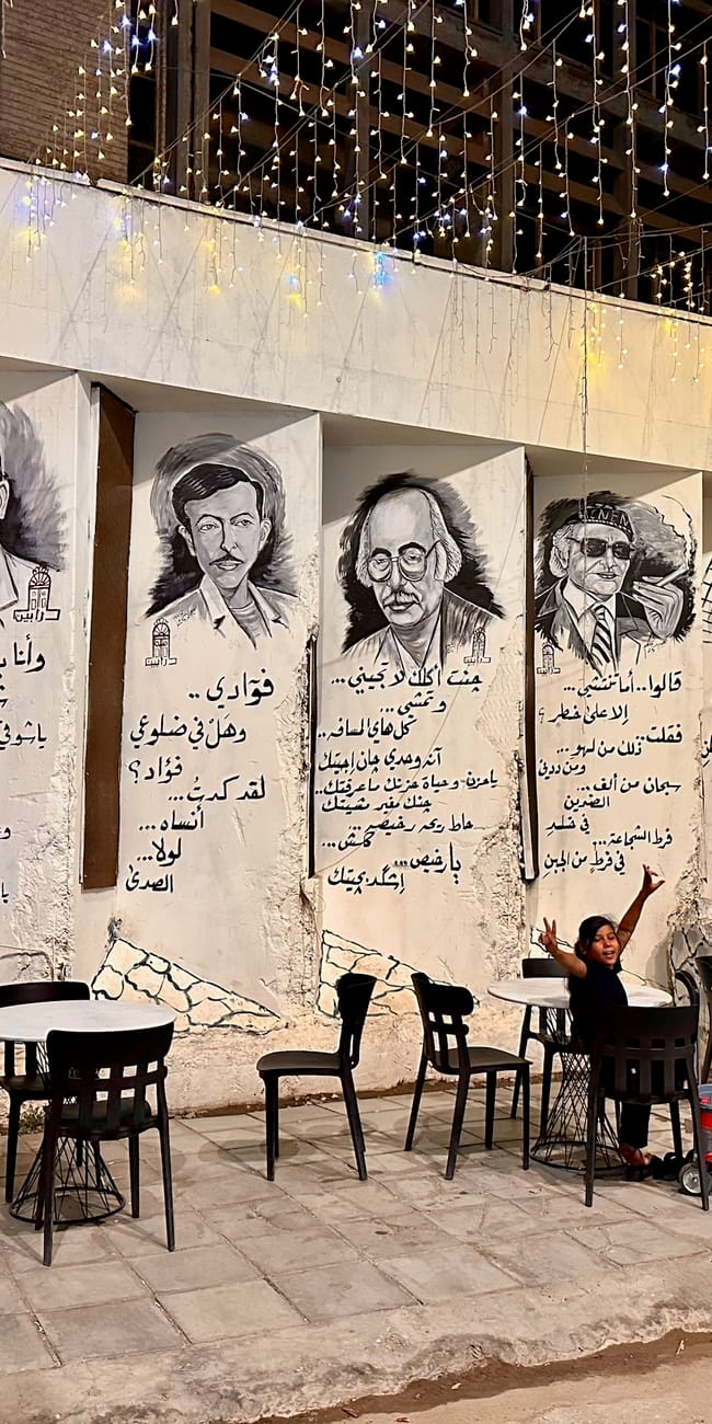 Kawiarnia w bagdadzie z muralami po arabsku i portretami na ścianie, przy stolikach siedzą ludzie