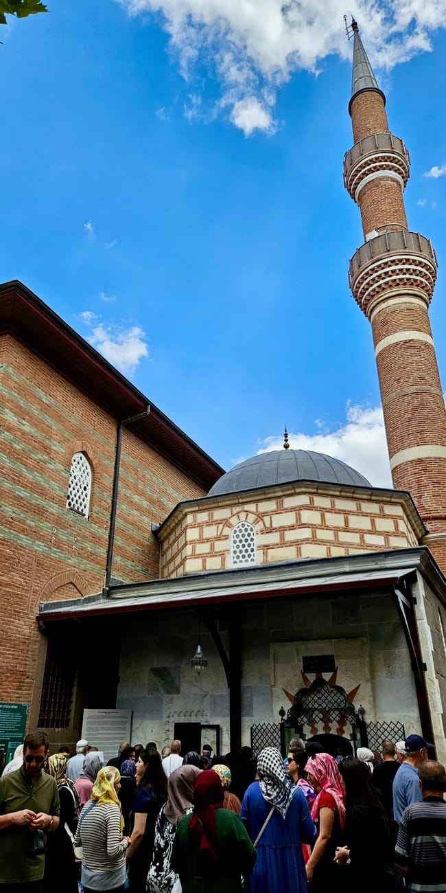 Crowd visiting ankara mayram mosque in turkey, with a tall minaret and gray dome against a blue sky