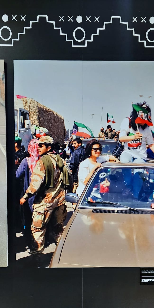 Visitors view kuwait city national museum display photos of armed vehicles and crowds with flags