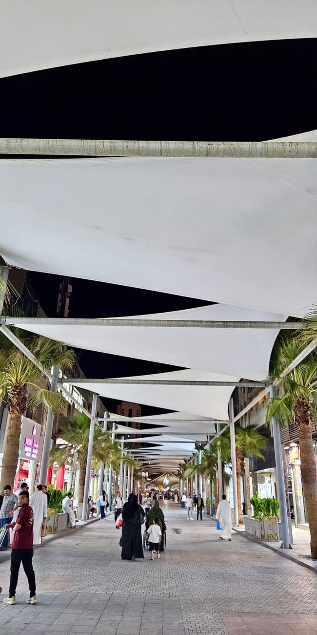 Kuwait, city al mubarakiya, covered walkway with white canopies and palm trees along a busy market street