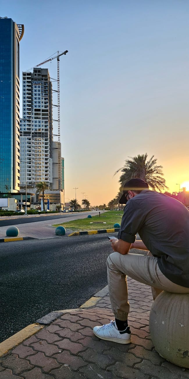 Kuwait city street photo with modern high-rise buildings at sunset and a man taking notes near the road