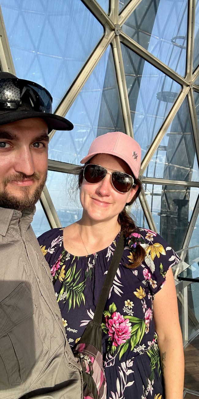Couple posing inside kuwait city towers with city views through the glass dome structure.