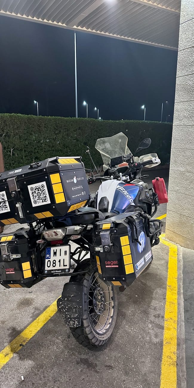 Motocykl podróżny z kuframi zaparkowany nocą przy noclegu w muskacie w omanie.