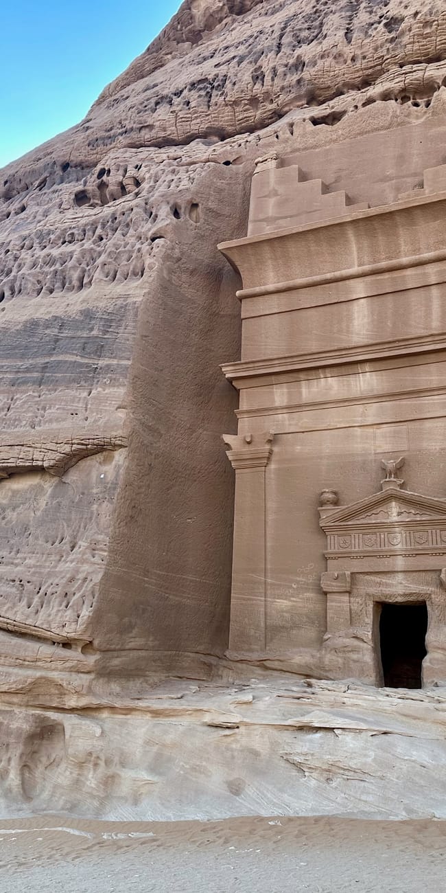 Saudi arabia, al ula hegra: sandstone tomb facade set into a rocky cliff with an arched doorway