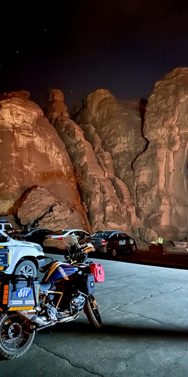 Motorcycle parked at al ula at midnight with cars in front of towering desert rocks in saudi arabia