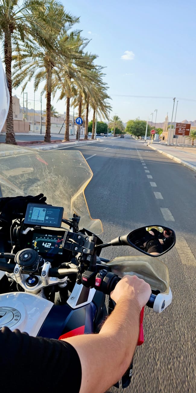 Rider on a motorcycle in al ula, saudi arabia, with palm-lined streets ahead