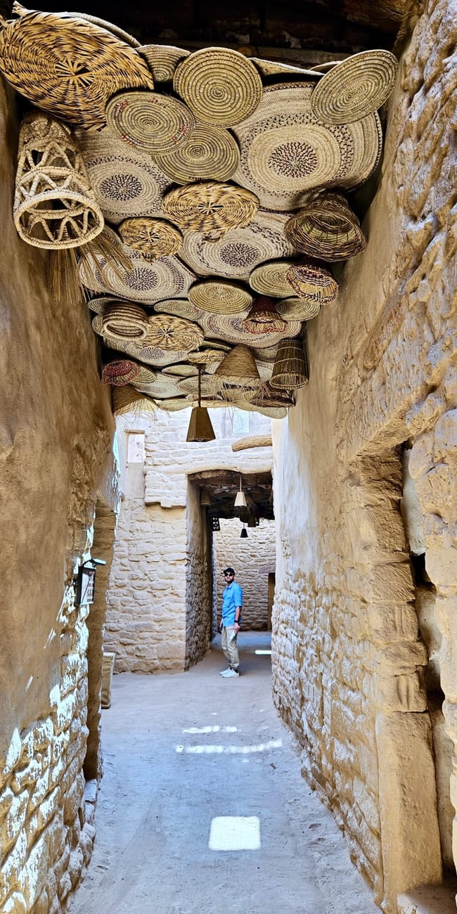 Al ula old town, saudi arabia, narrow stone passage with hanging woven baskets above a visitor