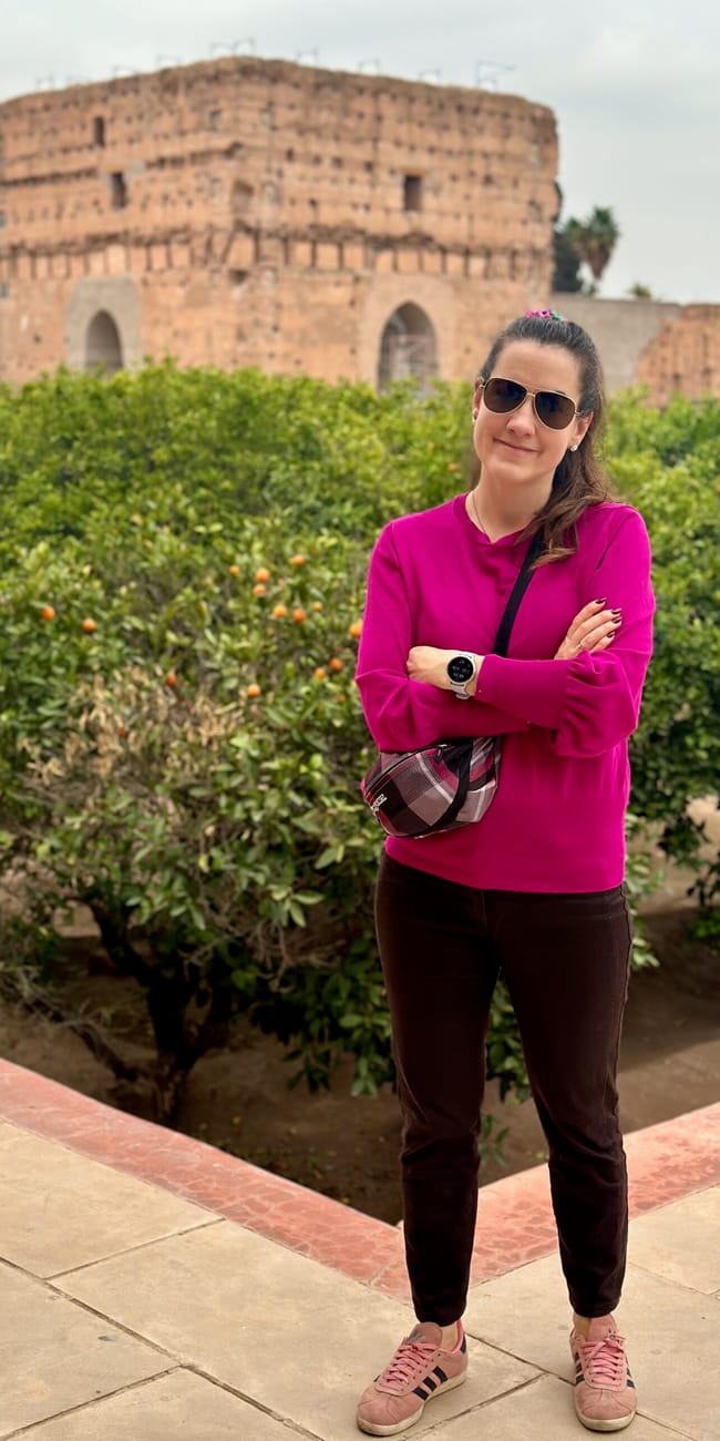 Woman in a bright pink top posing in marrakech badi palace gardens with a round sandstone building in the background