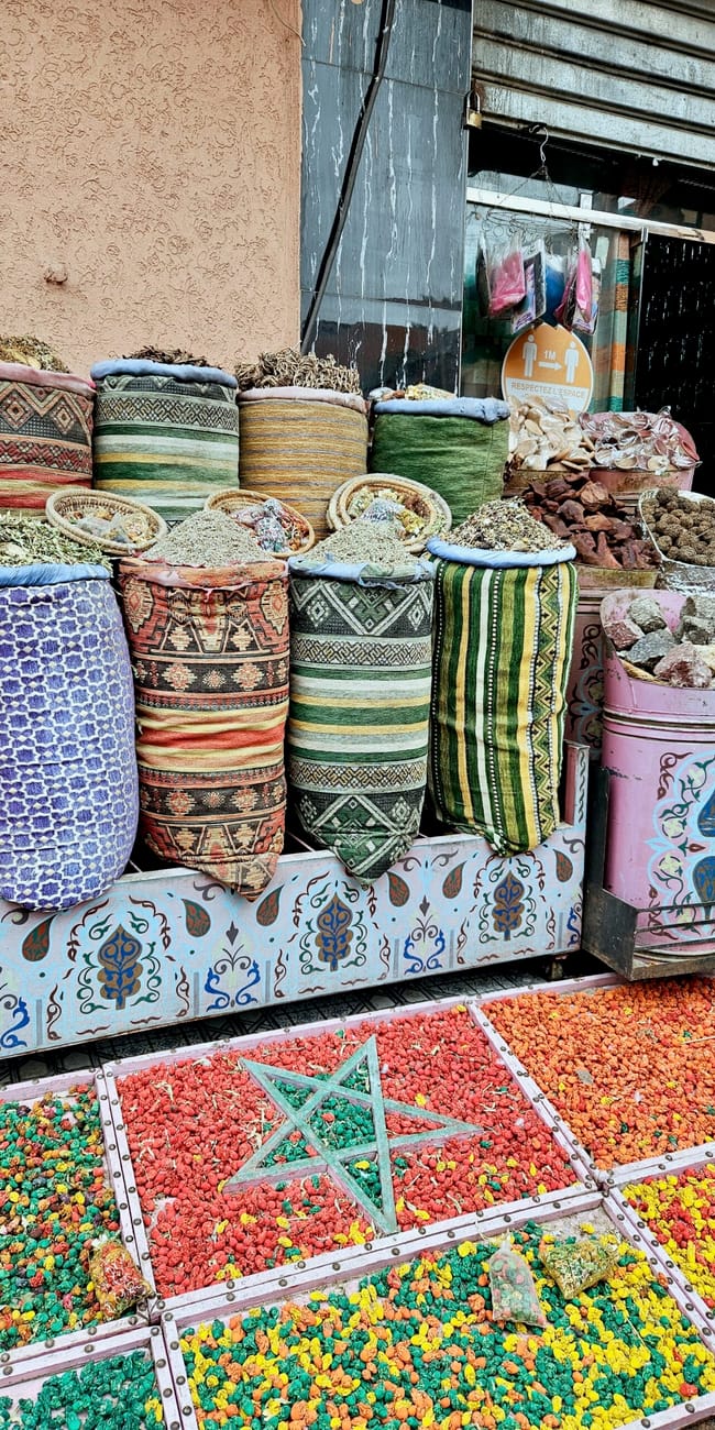 Morocco, marrakech bazaar: colorful spice and grain stalls with patterned sacks and jars in front of a shop.