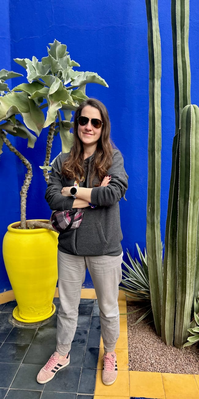 Marocco, marrakesz: jardin majorelle—woman posing beside tall cacti against bright blue walls