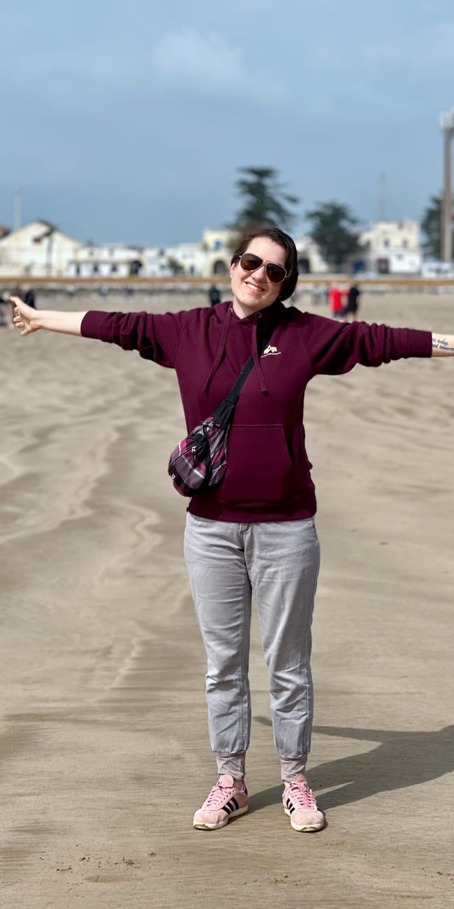 Essaouira, maroko: plaża w mieście, kobieta uśmiechnięta z rozłożonymi rękami na piasku