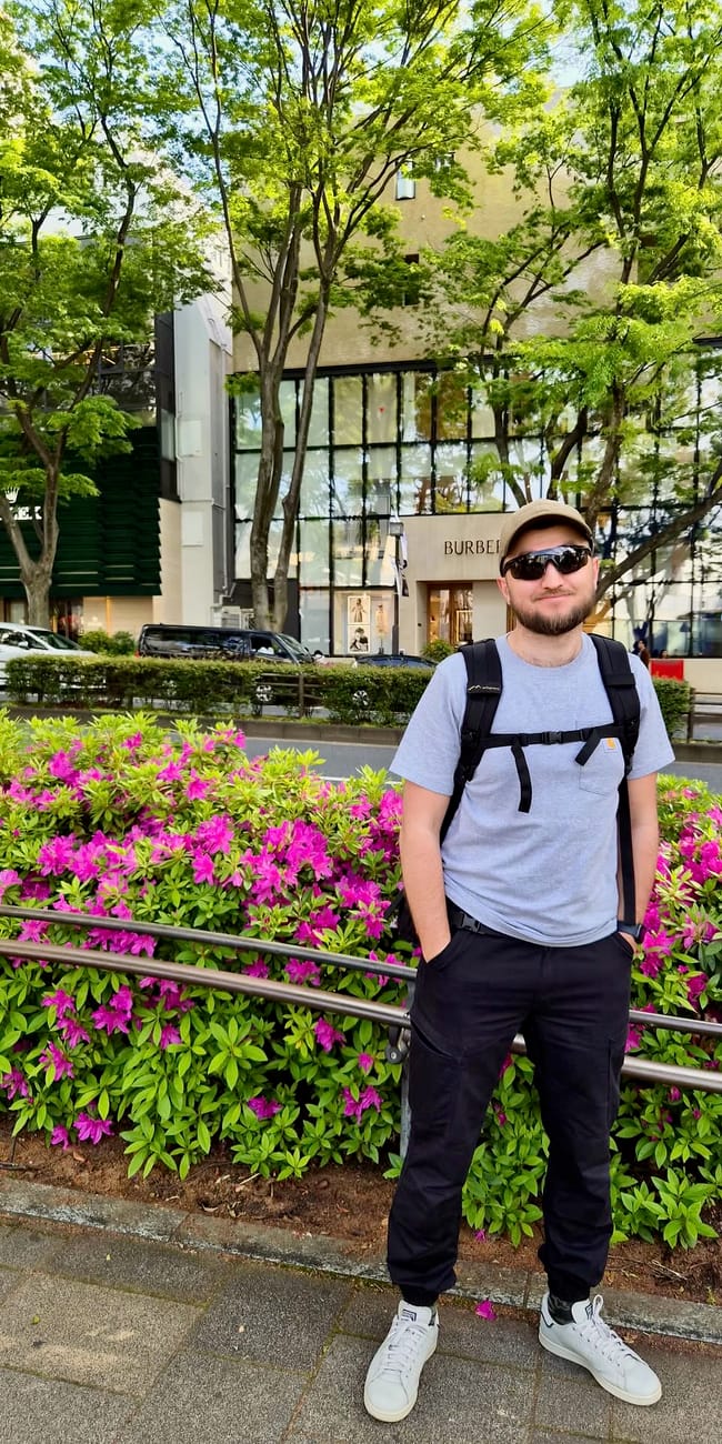 Filip stoi na ulicy w tokio przed sklepami burberry i rolex, otoczony zielenią i różowymi kwiatami