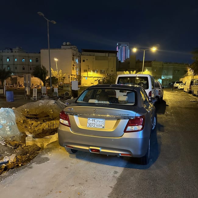 Szary sedan suzuki swift dzire zaparkowany nocą na ulicy w bahrajnie.