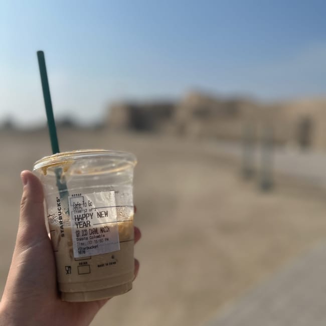 Kubek kawy starbucks trzymany na tle pustynnego krajobrazu w bahrajnie