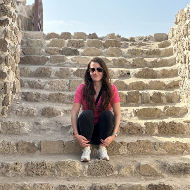 Bahrain fort: kobieta siedzi na kamiennych schodach pod błękitnym niebem.