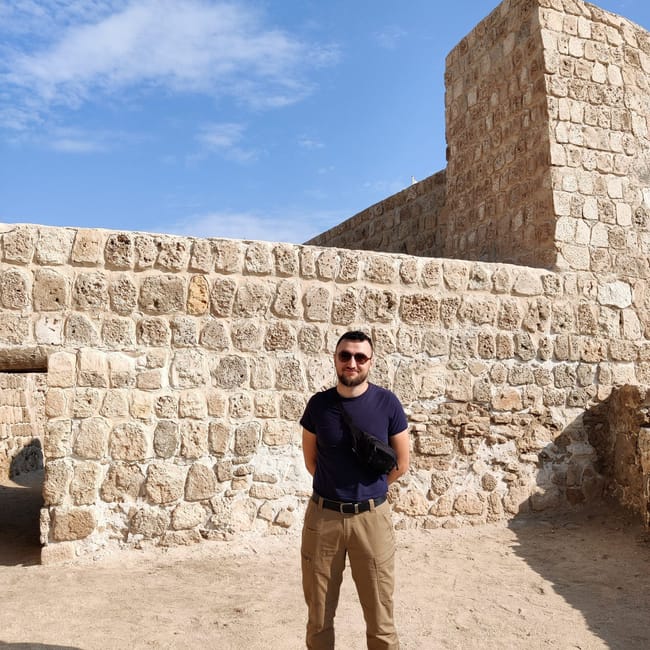Bahrain fort: mężczyzna stoi przed kamiennymi murami zabytkowej twierdzy pod błękitnym niebem.