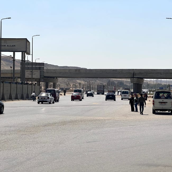 Road in egypt under an overpass, with cars, pedestrians, and desert hills in the background
