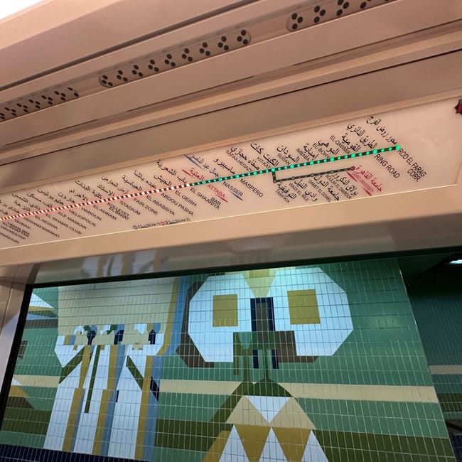Inside an egypt metro car with a route map and geometric window mural.