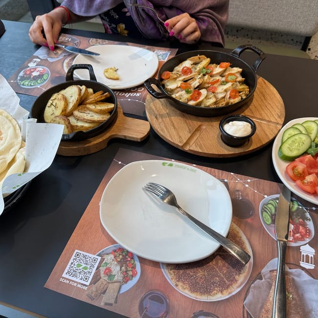 Egyptian meal with flatbreads, roasted potatoes, chicken, and sliced cucumbers and tomatoes on a table