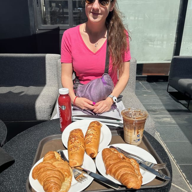 Woman at a café table in egypt with pastries, sandwiches, and iced coffee.
