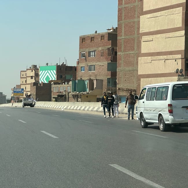 Road in safety, egypt, with apartment buildings, vans, and pedestrians.