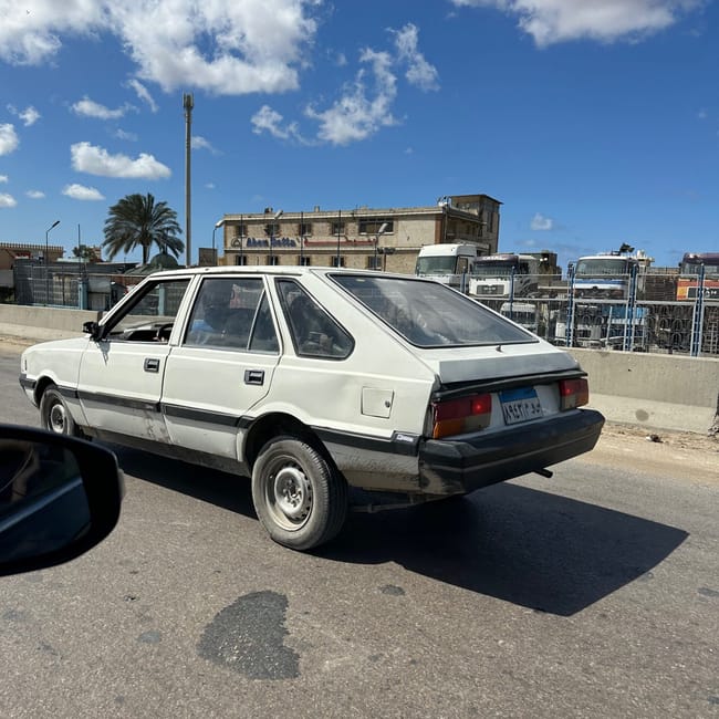 Old white sedan on a road in egypt under a blue sky with clouds.
