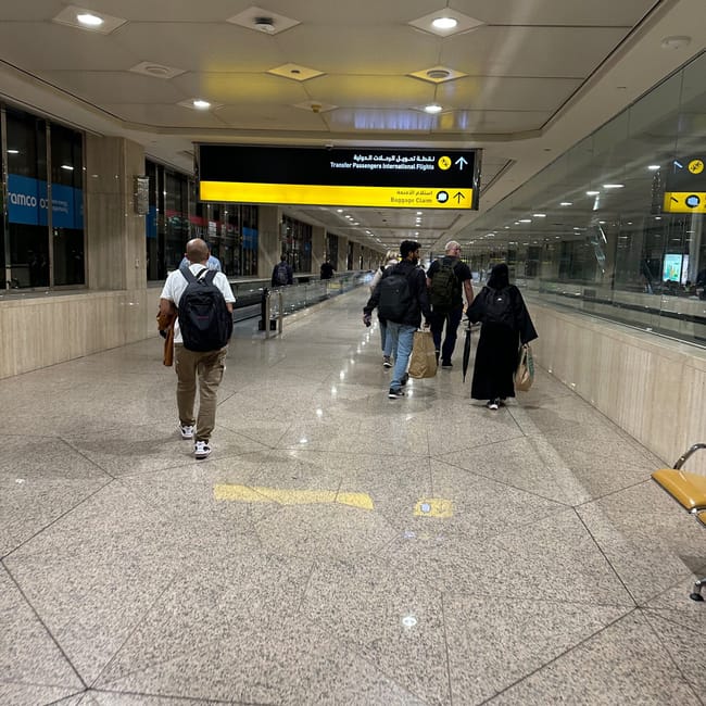Korytarz lotniska w arabii saudyjskiej z podróżnymi i znakami do odbioru bagażu oraz tranzytu.