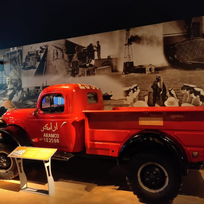 Czerwony zabytkowy pickup aramco w ithra w dammam, obok planszy historycznej.