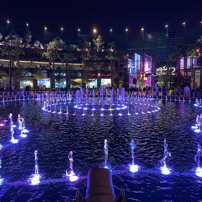 Riyadh boulevard world nocą, podświetlone fontanny i kolorowe neony przy promenadzie