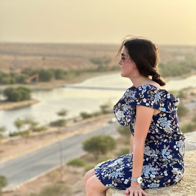 Riyadh al-hayer park lake: kobieta siedzi na skale z widokiem na jezioro i pustynny krajobraz.