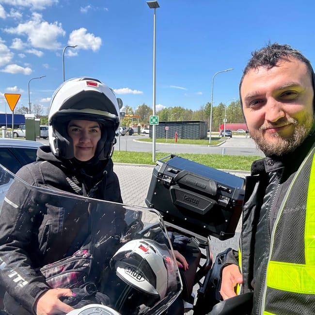 Para motocyklem w wiedniu, dwoje osób w kaskach robi selfie przy motocyklu.