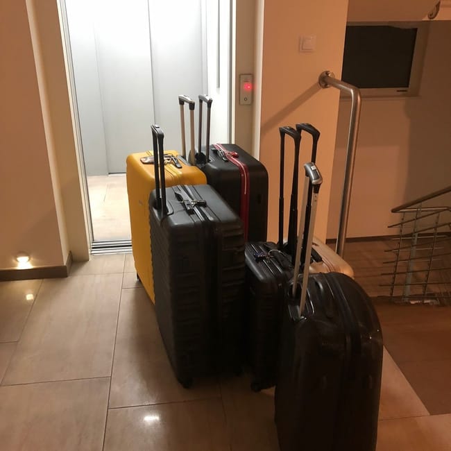 Pięć walizek ustawionych przed windą w hotelowym wnętrzu, w tym uszkodzona bagażowa.
