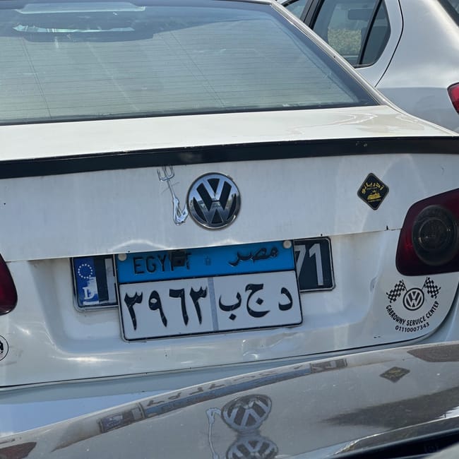 Tył białego volkswagena z egipską tablicą z europejskim oznaczeniem w kairze.