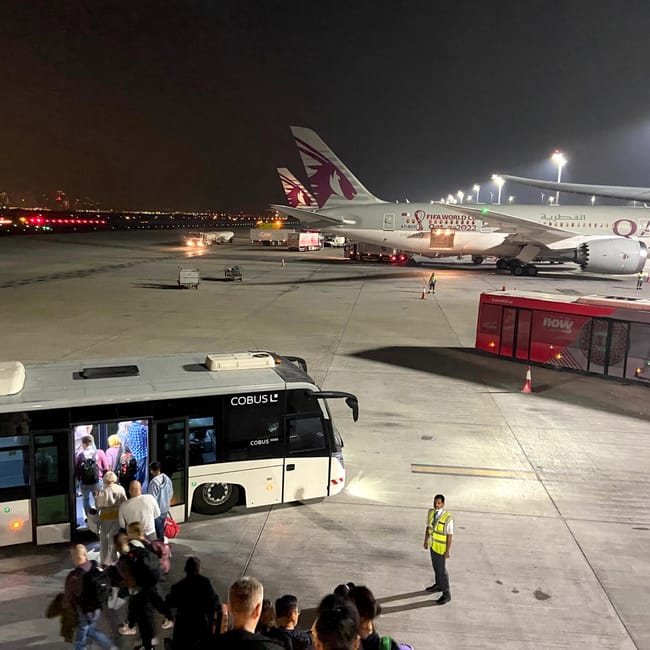 Pasażerowie wsiadają do autobusu na płycie lotniska obok samolotu qatar airways nocą.
