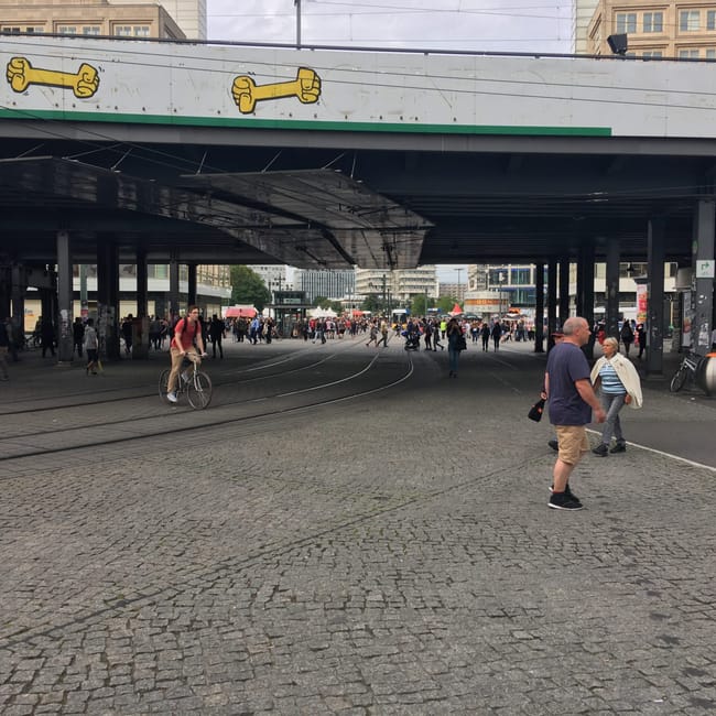 Przejście pod wiaduktem w berlinie, z pieszymi, rowerzystą i graffiti z żółtymi kośćmi.