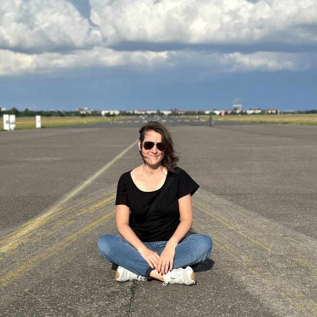 Kobieta siedzi na pasie startowym na lotnisku tempelhof w berlinie, pod dramatycznymi chmurami.