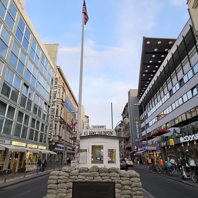 Checkpoint charlie w berlinie z dawną strażnicą i masztem z flagą usa, między nowoczesnymi budynkami.