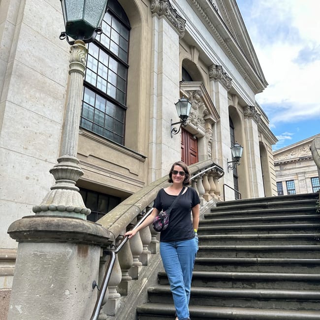 Gendarmenmarkt w berlinie, przed klasycystycznym budynkiem na schodach stoi kobieta.