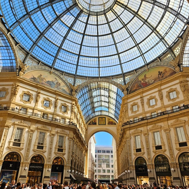 Galleria vittorio emanuele ii w mediolanie z przeszkloną kopułą i tłumem ludzi.