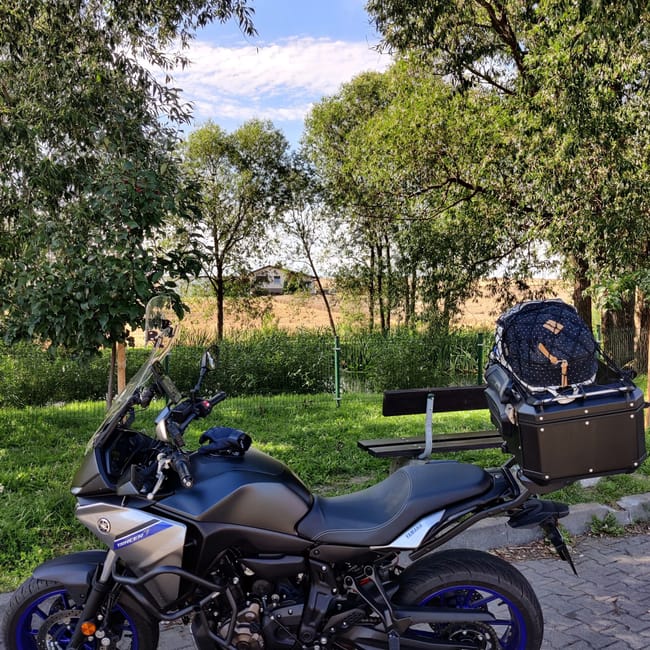 Motocykl yamaha tracer 7 zaparkowany w szczecinie przy parku i ławce, z kufrem i bagażem na tylnej części.