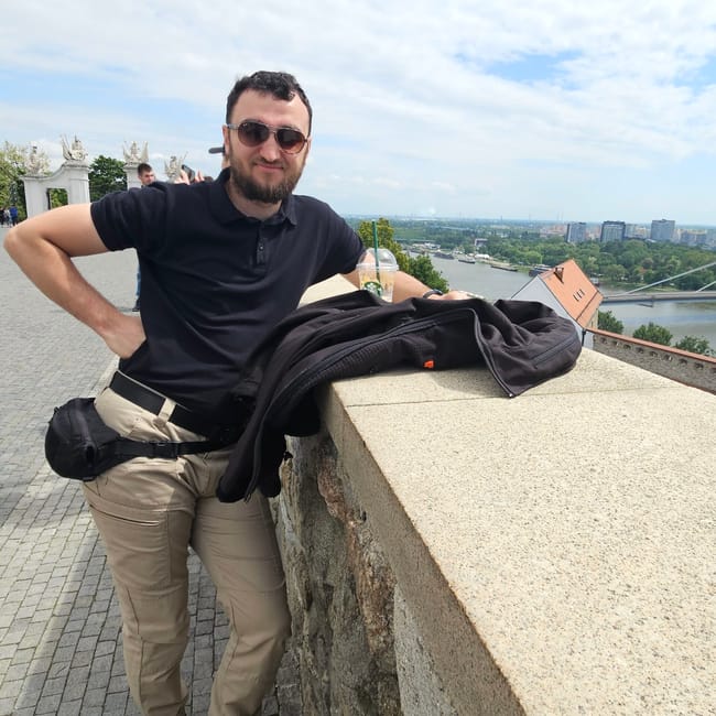 Mężczyzna przy murze zamkowym w bratysławie, z widokiem na panoramę miasta i rzekę.