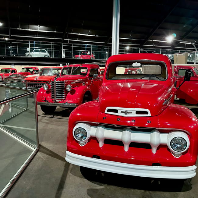 Red classic cars on display at uae, abu dhabi emirates national auto museum, viewed in a bright gallery.