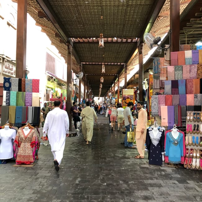 Bazar w dubaju z kolorowymi tkaninami i ubraniami przy krytym pasażu.
