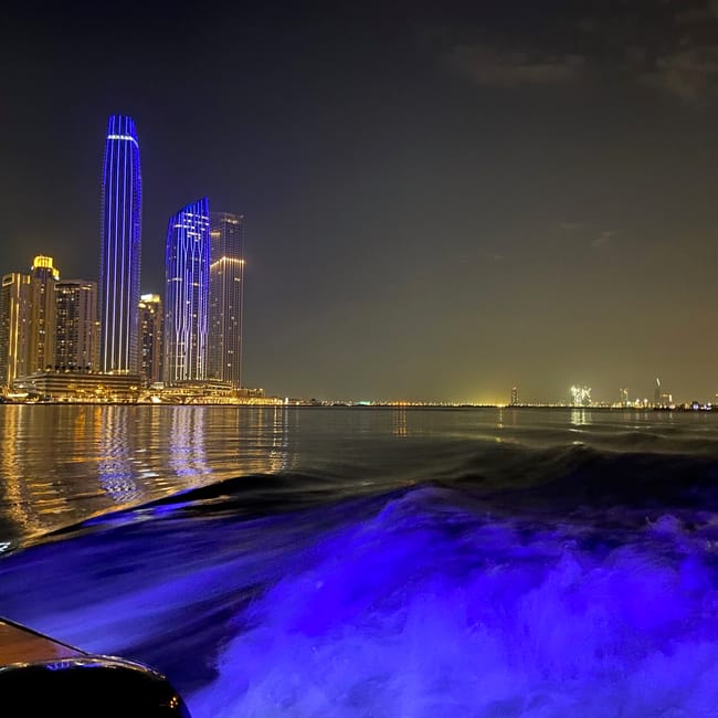 Dubai creek nocą z podświetlonymi wieżowcami i śladami łodzi na wodzie