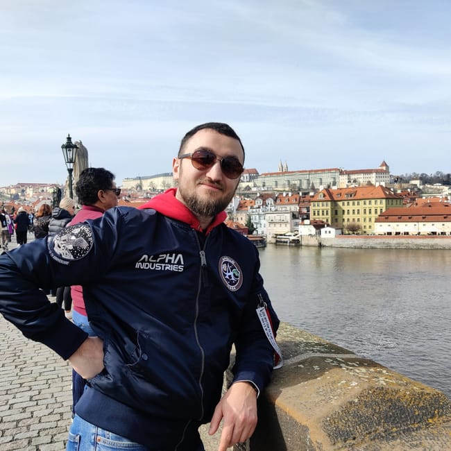 Mężczyzna stoi na moście karola w pradze nad wełtawą, w tle zabytkowa panorama miasta.
