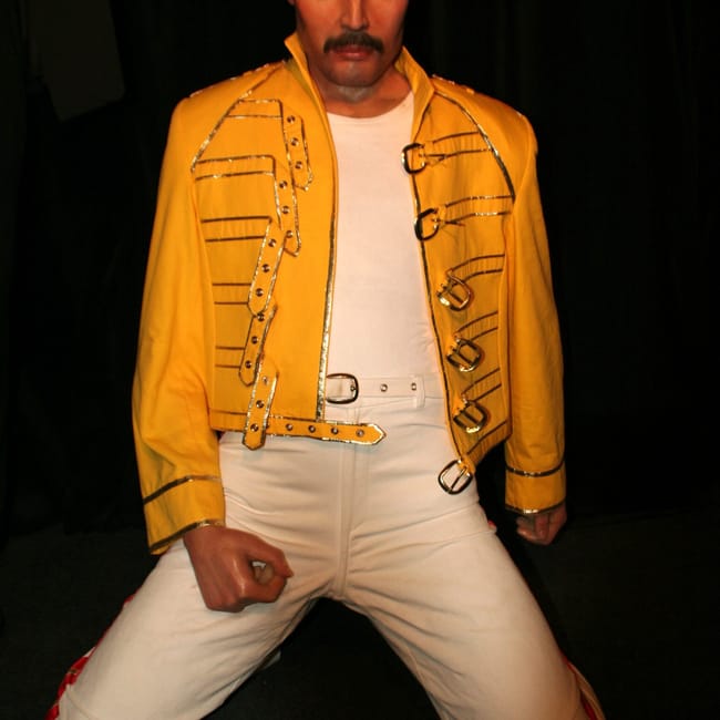 Figura woskowa freddiego mercury’ego w madame tussauds w pradze, w żółtej kurtce i białych spodniach.