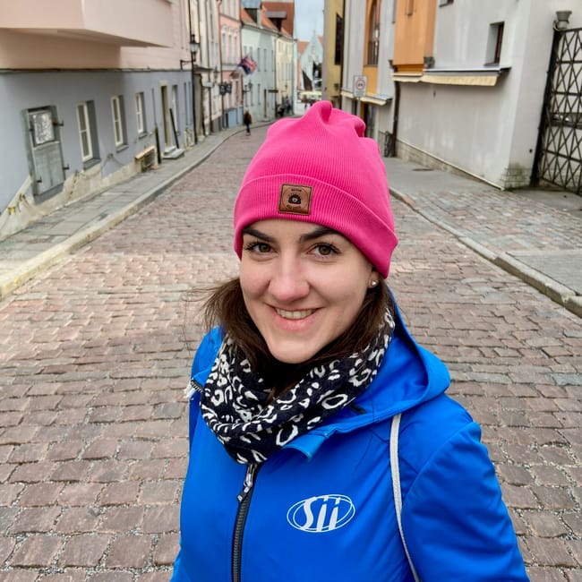 Smiling woman in tallinn, estonia wearing a pink beanie and blue jacket on a cobblestone street