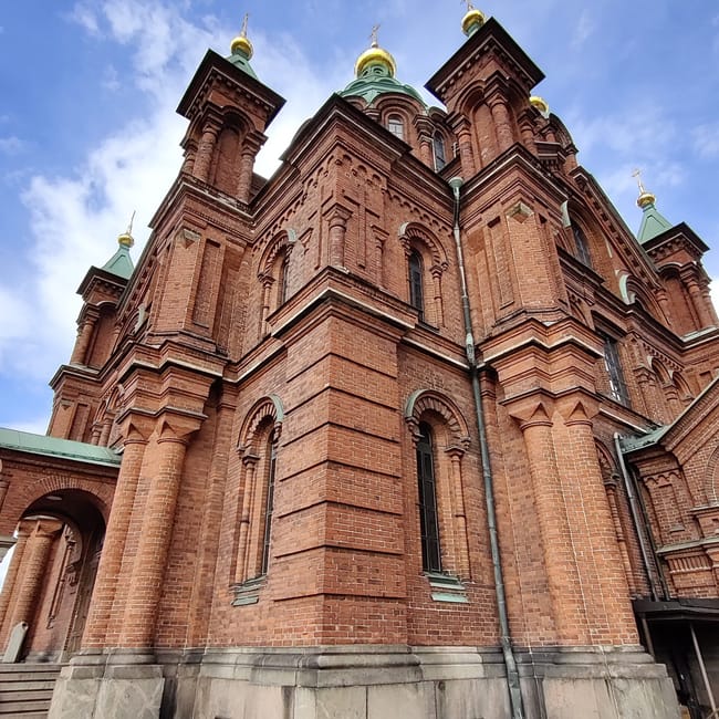 Katedra uspieńska w helsinkach z czerwonej cegły i złotymi kopułami na tle nieba